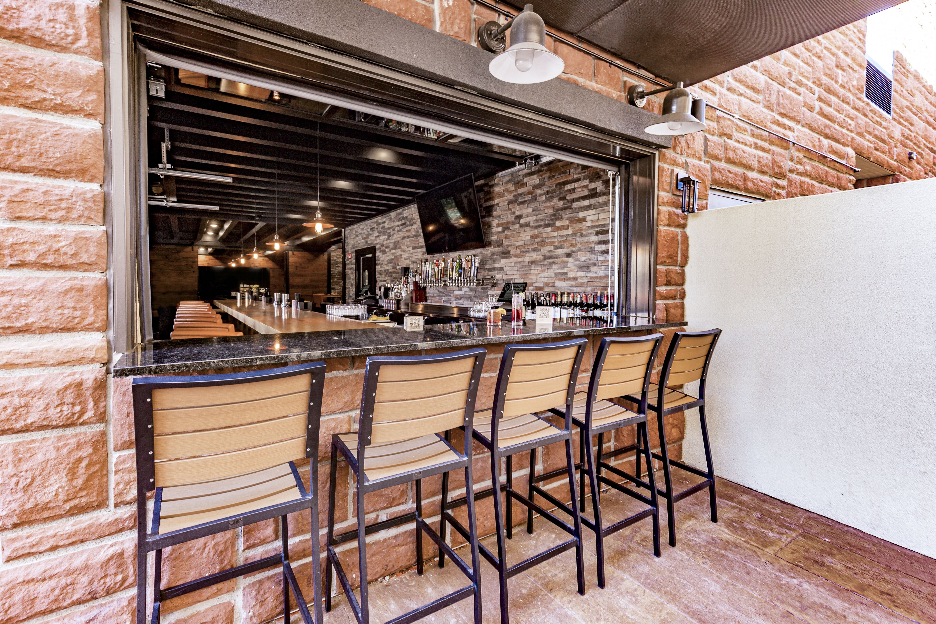 A bar area with a brick wall, wooden bar counter, and metal chairs.