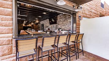 A bar area with a brick wall, wooden bar counter, and metal chairs.