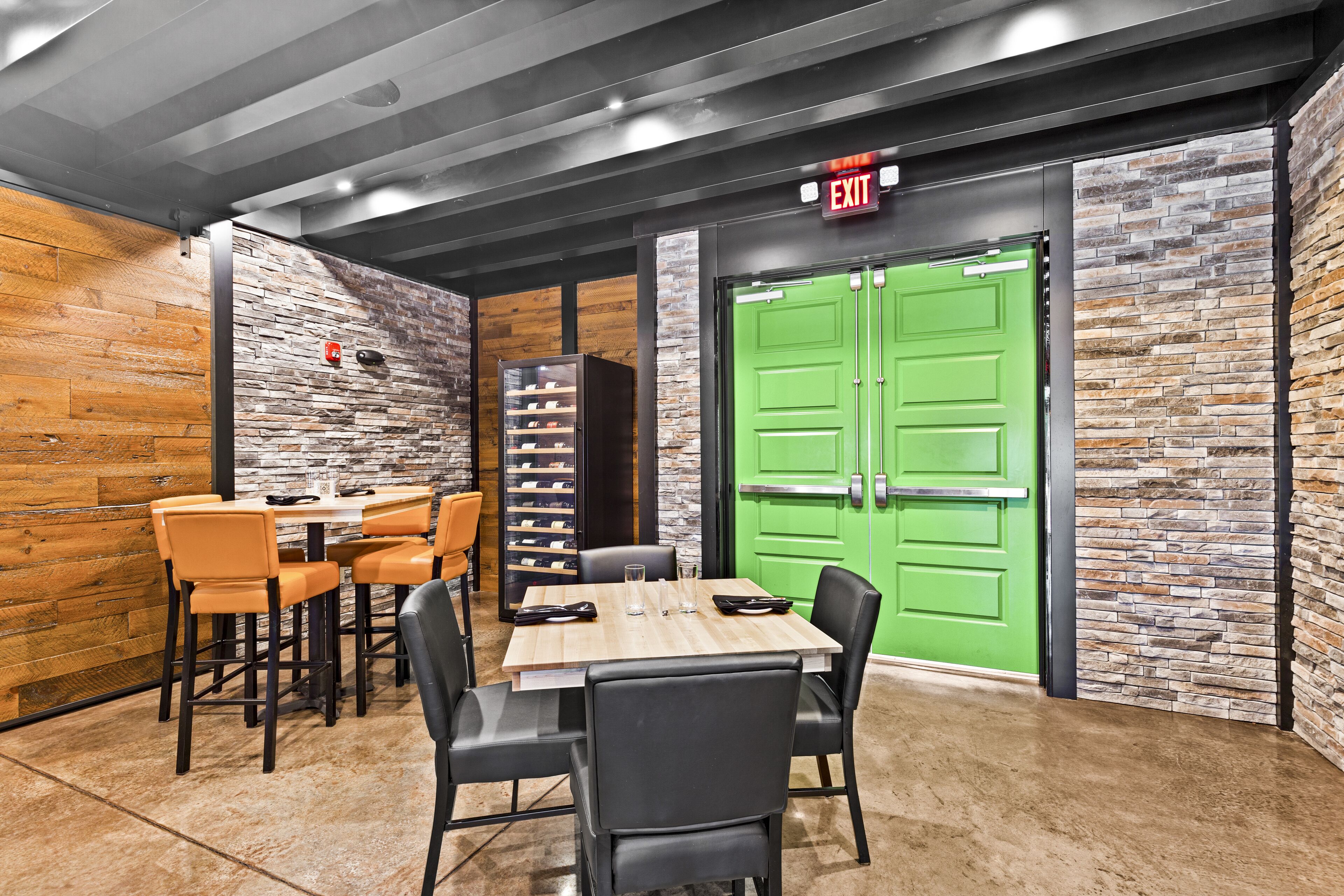 A dining area with a wooden table and black chairs, a green door, and a brick wall.