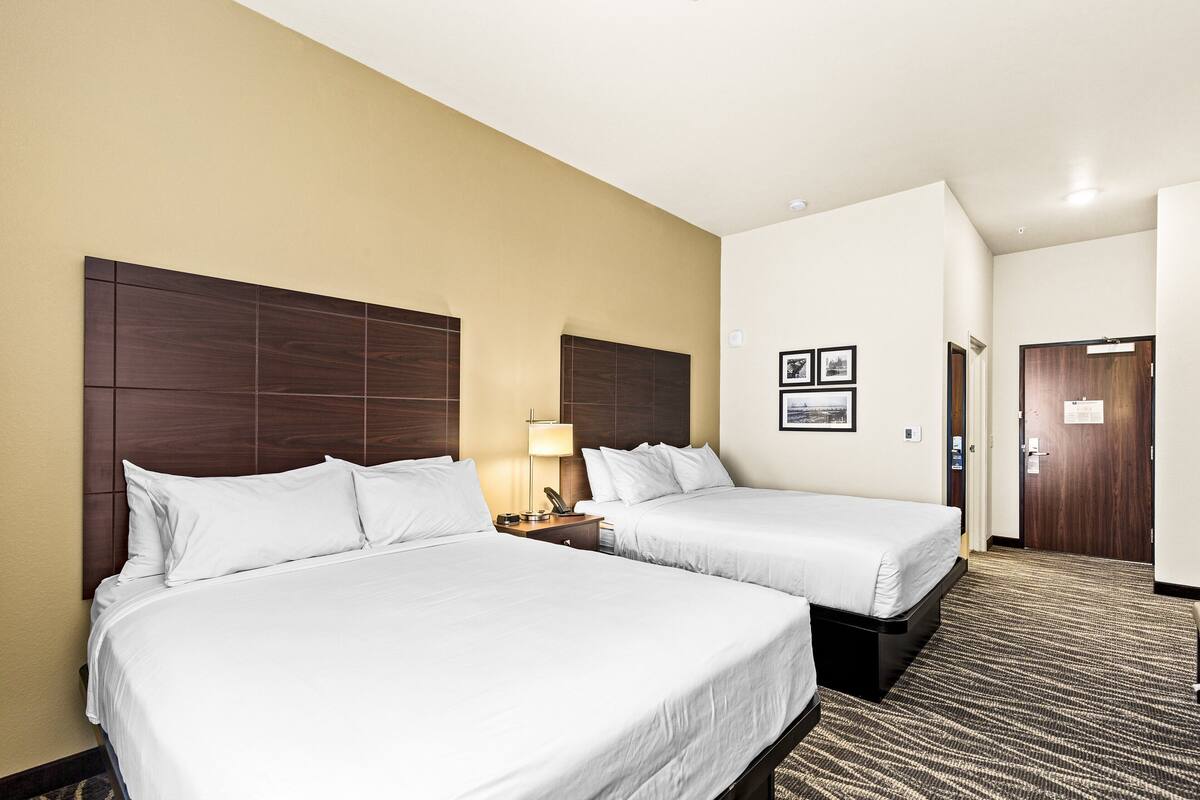 A hotel room with two beds, a nightstand, a lamp, and a door.