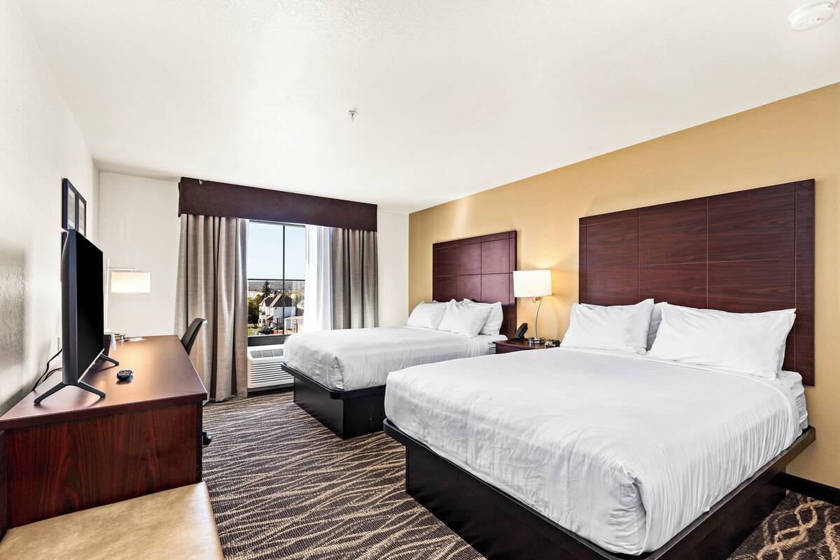 A hotel room with two beds, a desk, a TV, and a view of the outside.