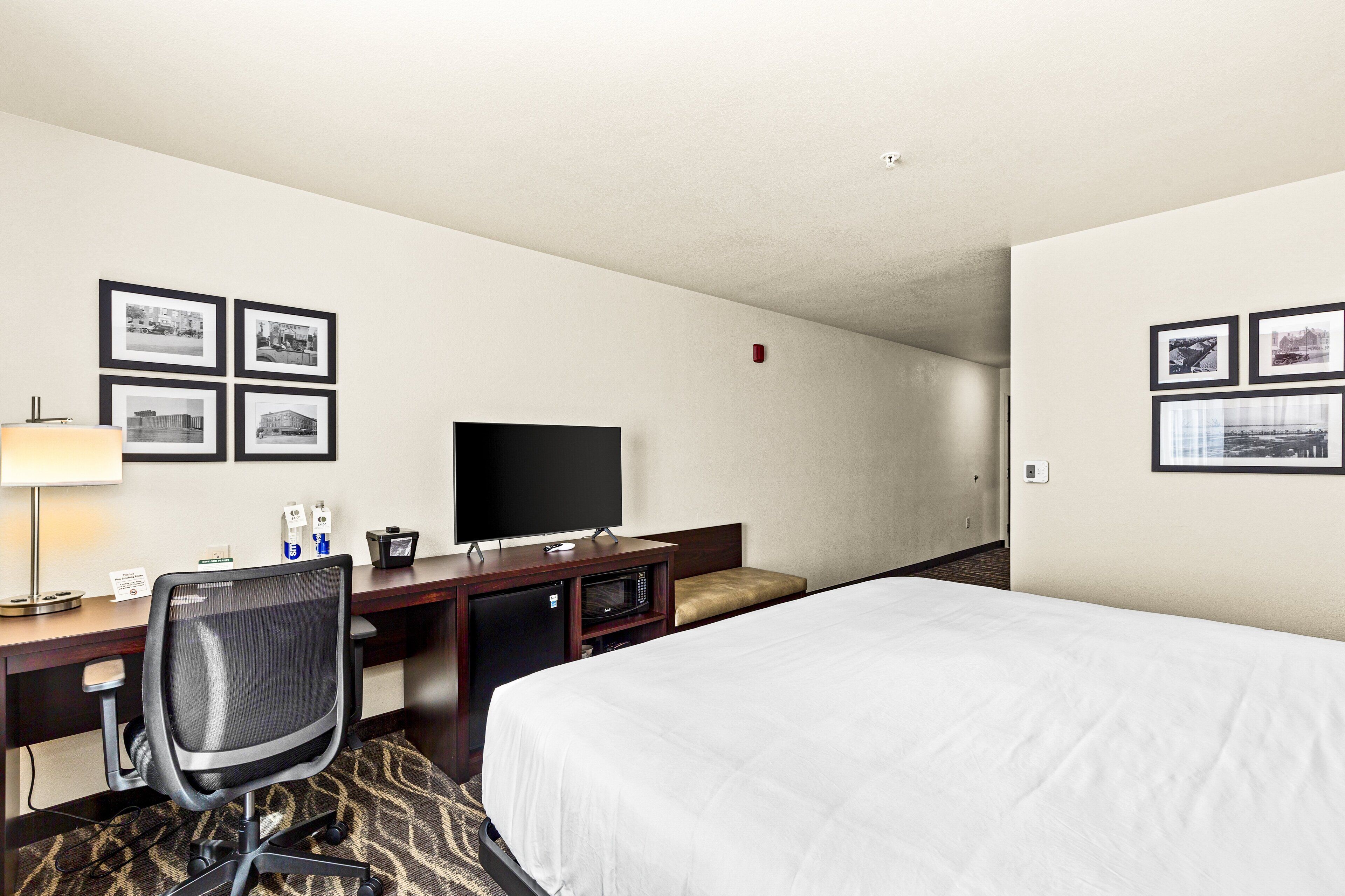 Una habitación de hotel con cama, escritorio, silla, televisor y cuadros en las paredes.
