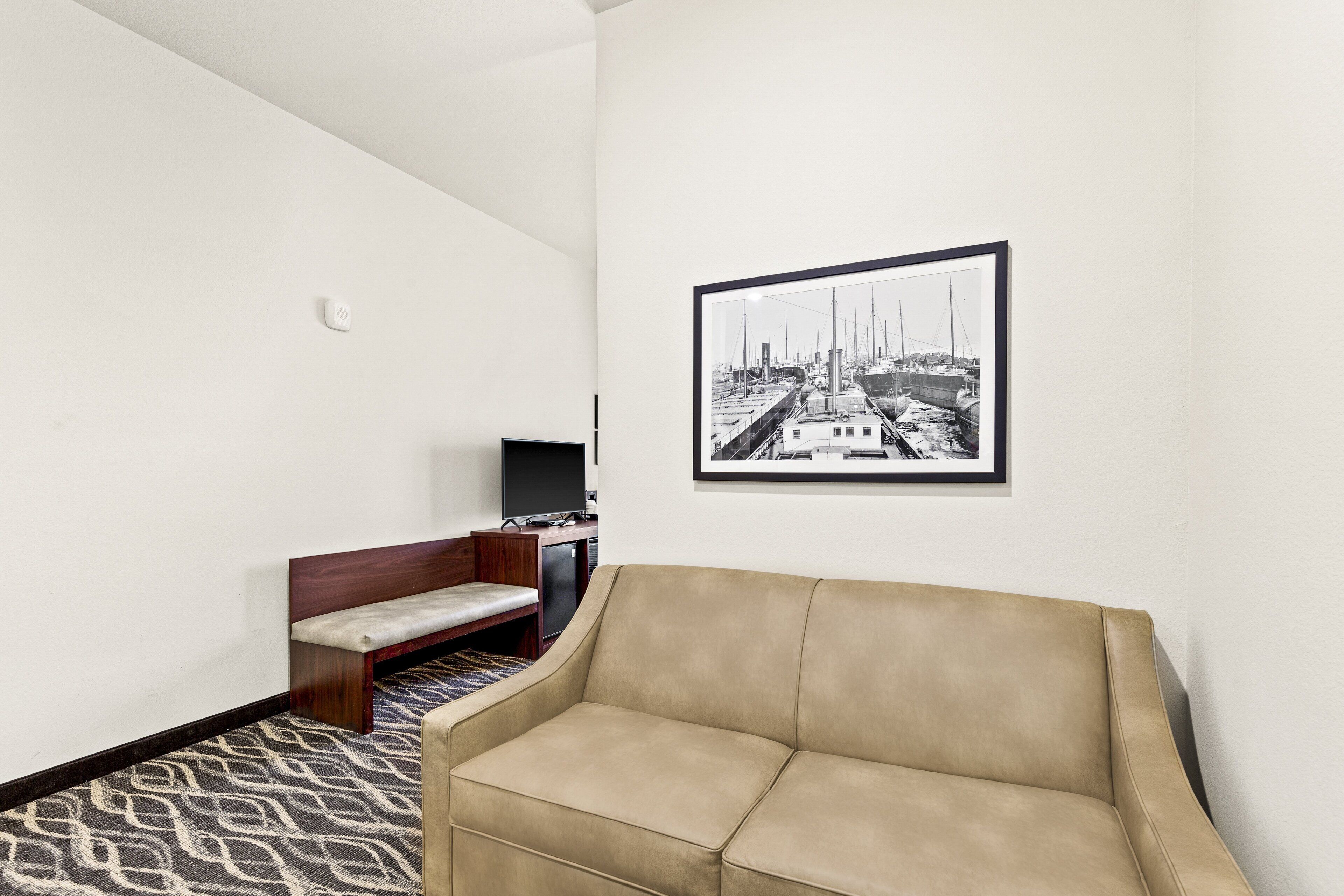 Una habitación con un sofá color crema, un banco de madera, un televisor de pantalla plana y una fotografía blanco y negro enmarcada en la pared.