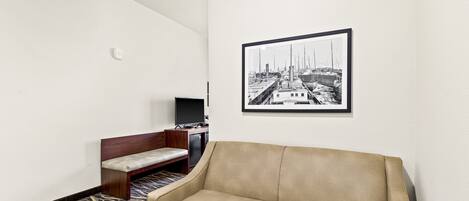 A room with a beige sofa, a wooden bench, a flat-screen TV, and a framed black and white photo on the wall.