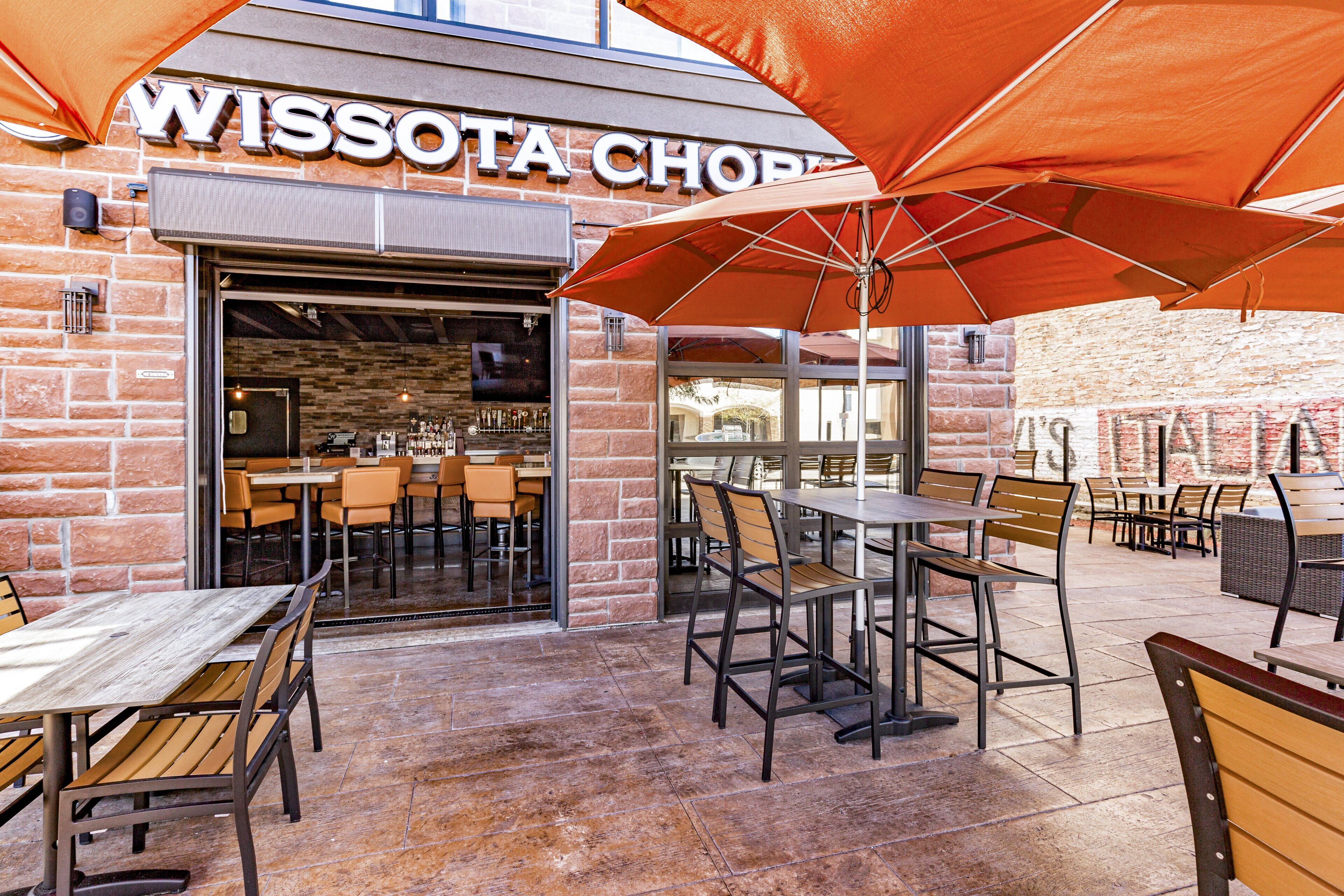 An outdoor seating area with tables and chairs, a brick wall, and a sign that reads "WISSOTA CHOPPY".