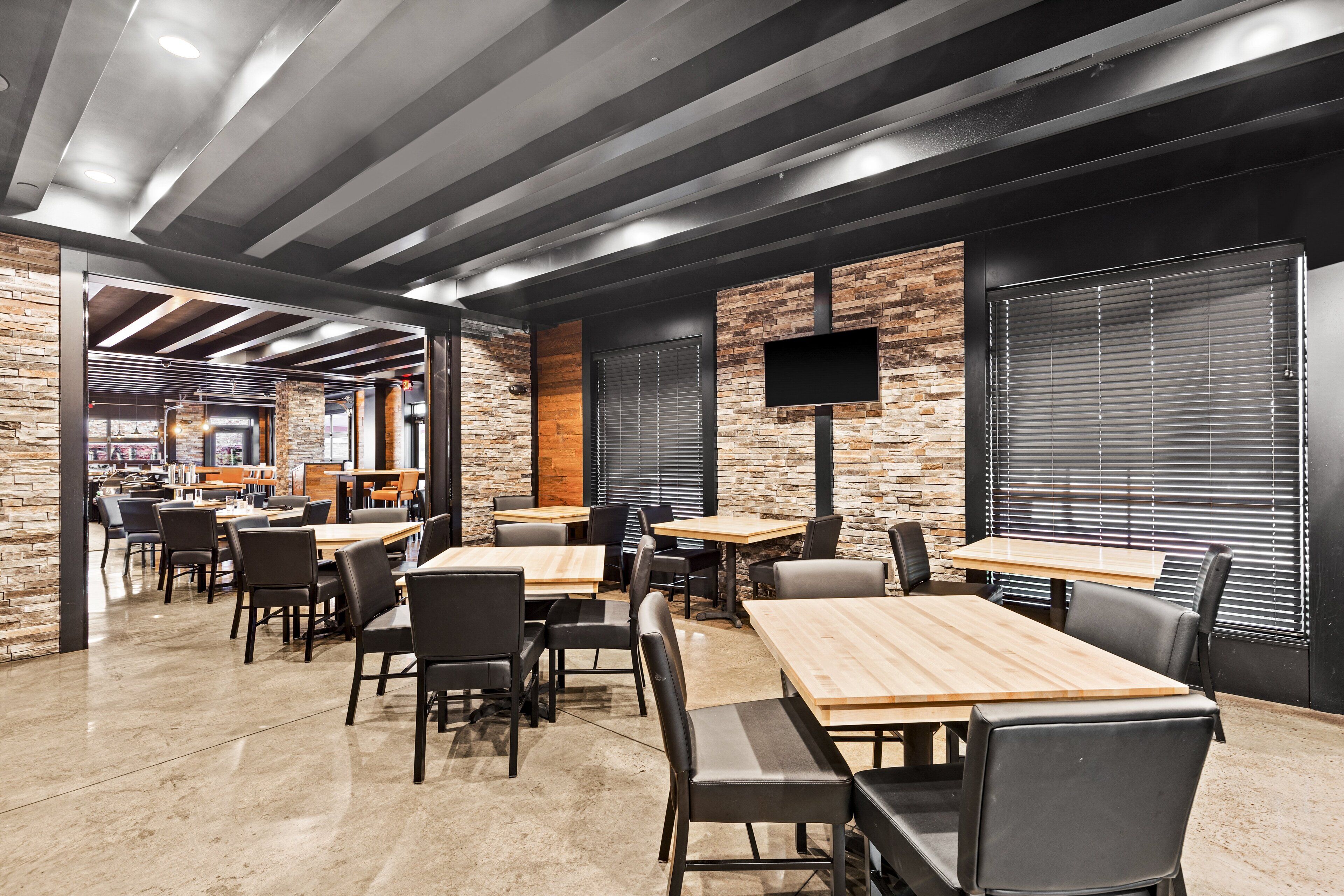 A modern restaurant interior with exposed ceilings, stone walls, and a mix of wooden and metal furniture.