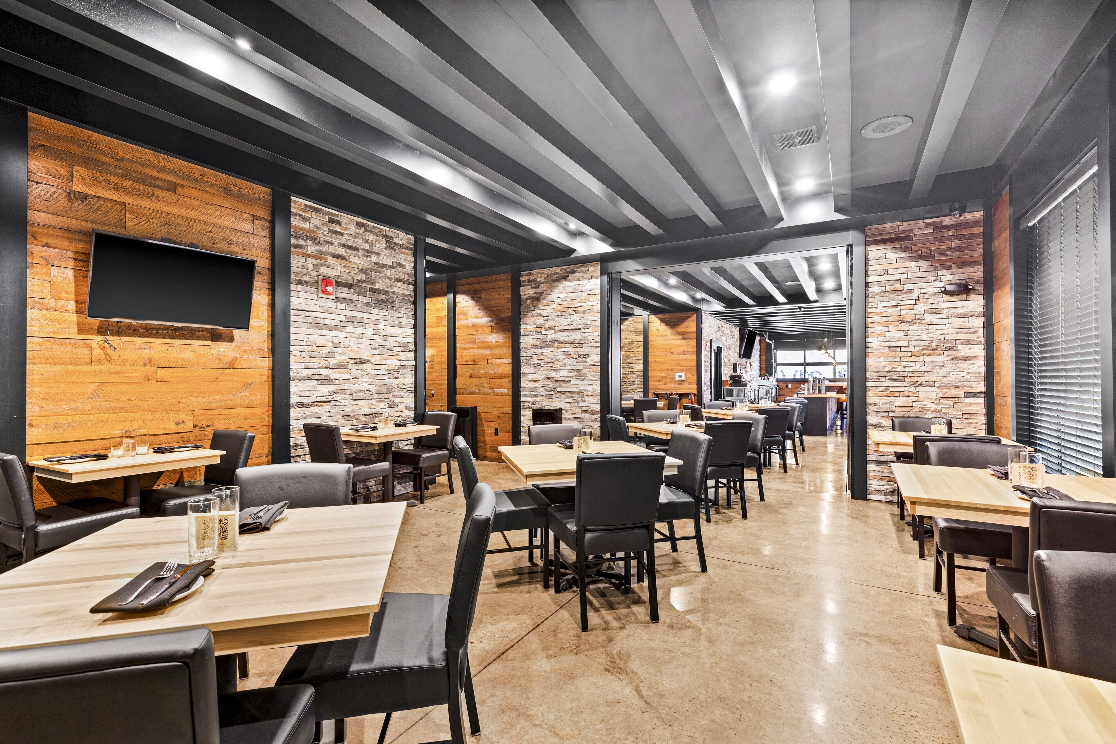 A modern restaurant with exposed brick walls, wooden accents, and a mix of table and booth seating.