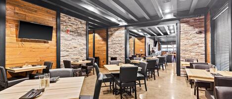 A modern restaurant with exposed brick walls, wooden accents, and a mix of table and booth seating.