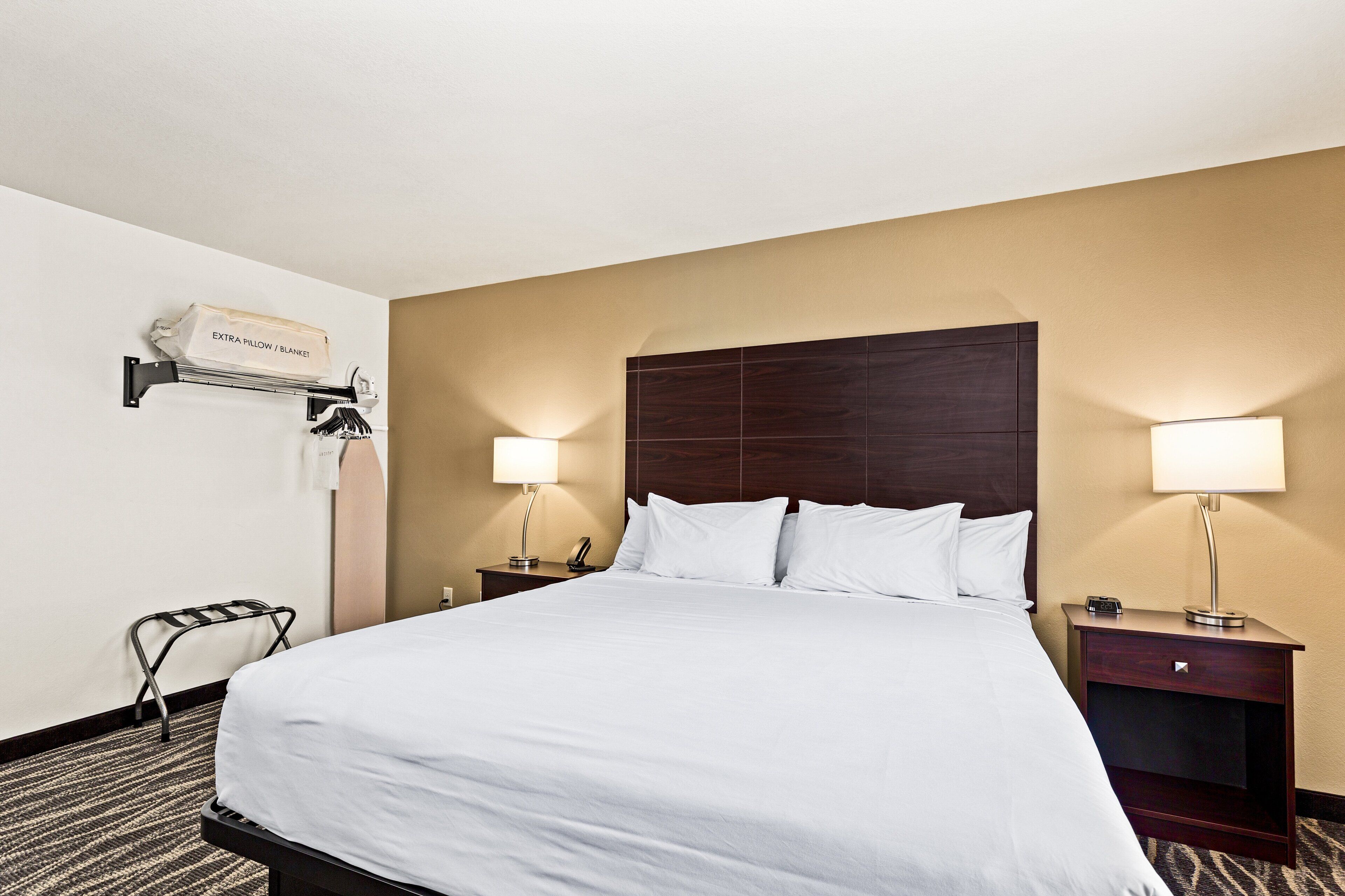 A hotel room with a large bed, two bedside tables with lamps, a wall-mounted air conditioner, and a small chair.