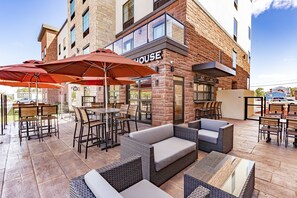 An outdoor patio area with wicker furniture, red umbrellas, and a brick building with a sign that reads "HOUSE". - Cobblestone Hotel & Suites - Superior Duluth (Superior)