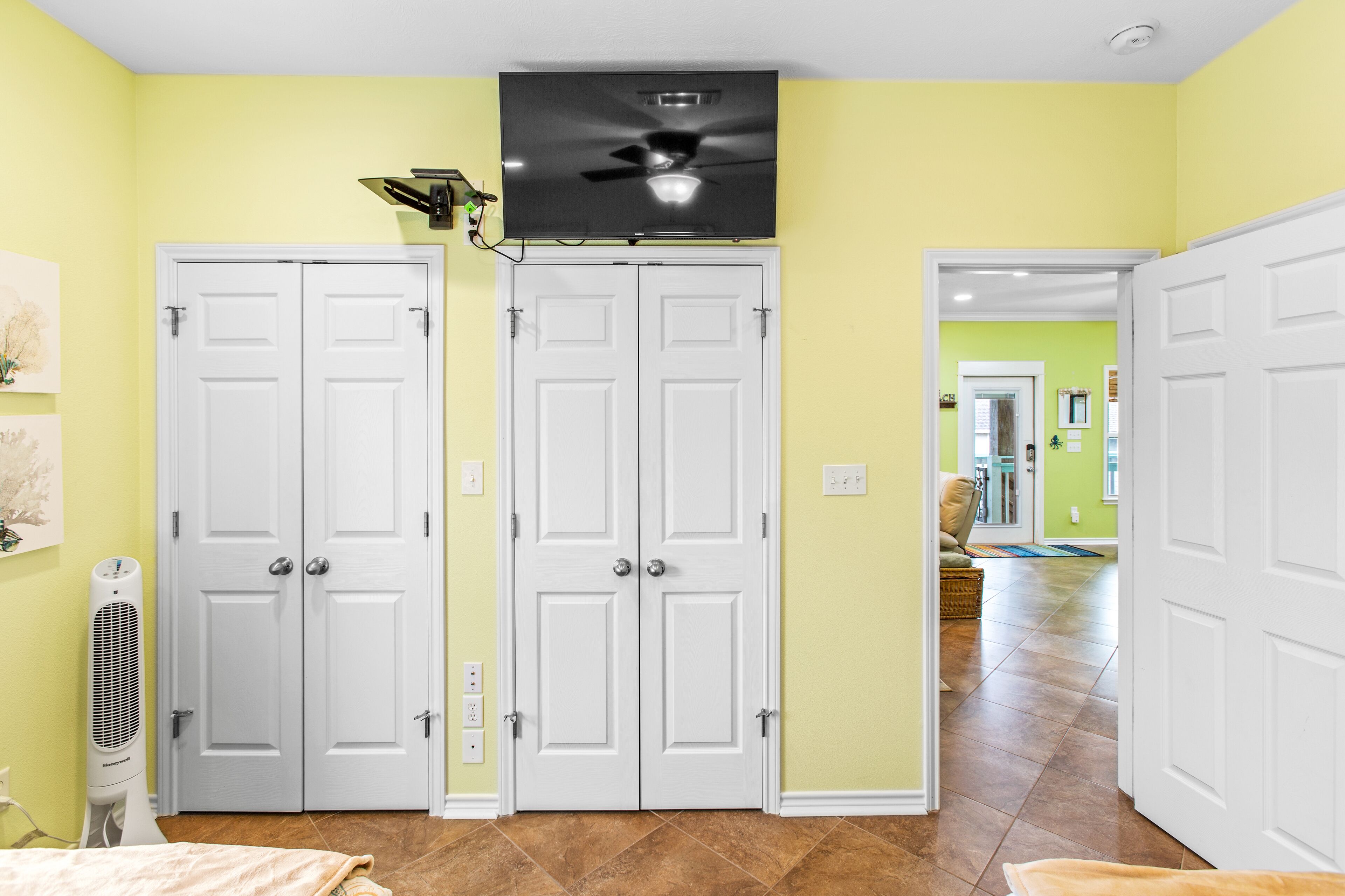 A room with two white doors, a ceiling fan, and a television mounted above.