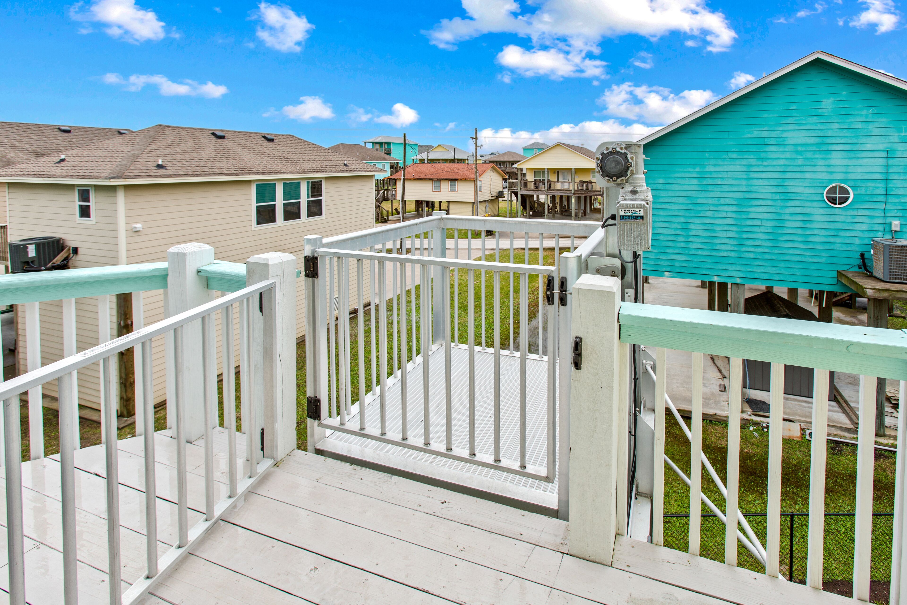 A wooden deck with a white railing leading to a house with a turquoise exterior.
