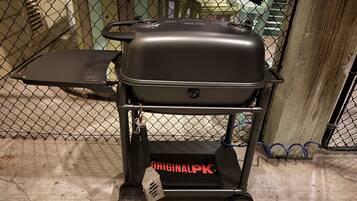 Un barbecue portatif, monté sur un chariot à roulettes, avec une clôture en mailles métalliques en arrière-plan.