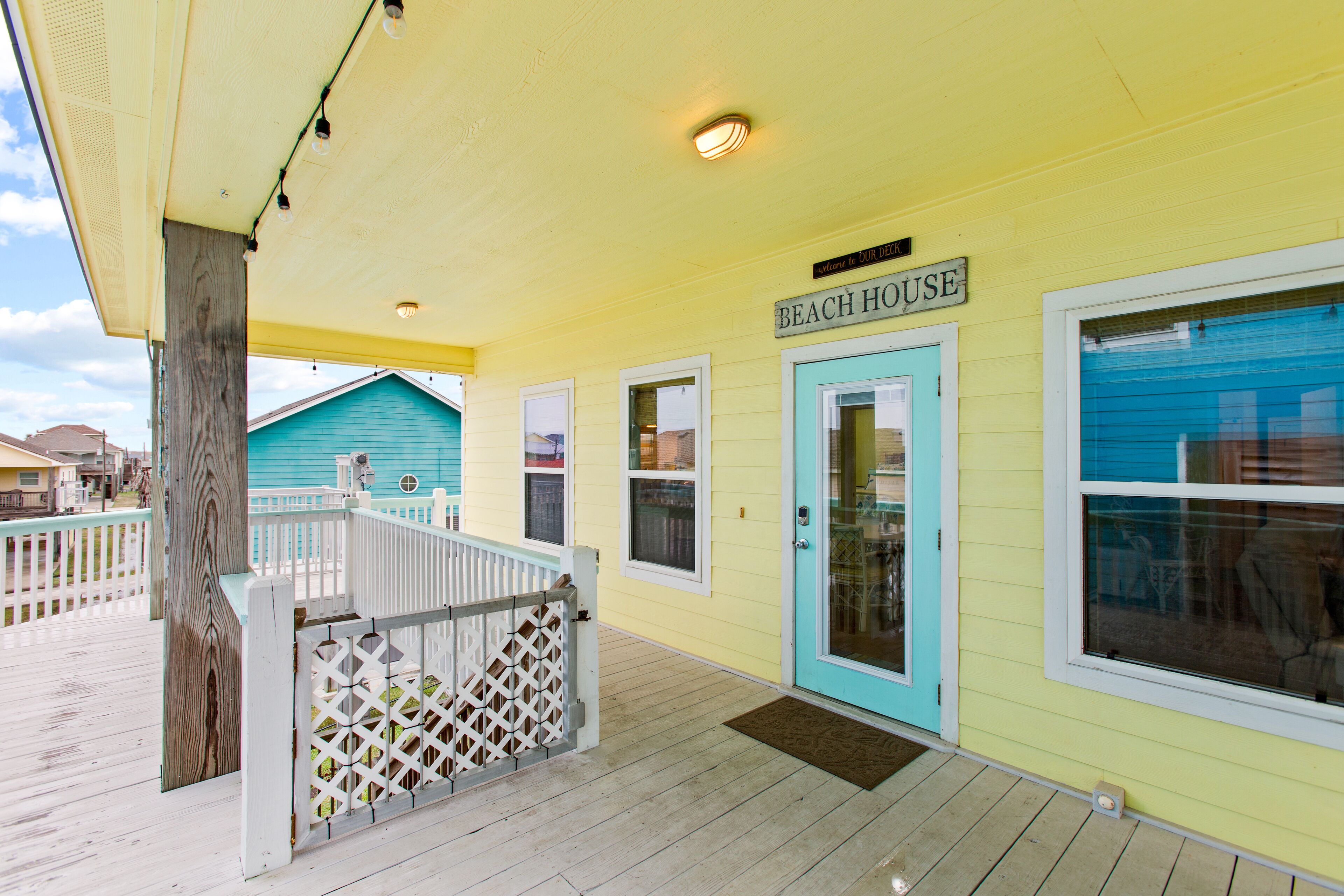 A beach house with a porch, a sign reading "BEACH HOUSE", and a blue door.
