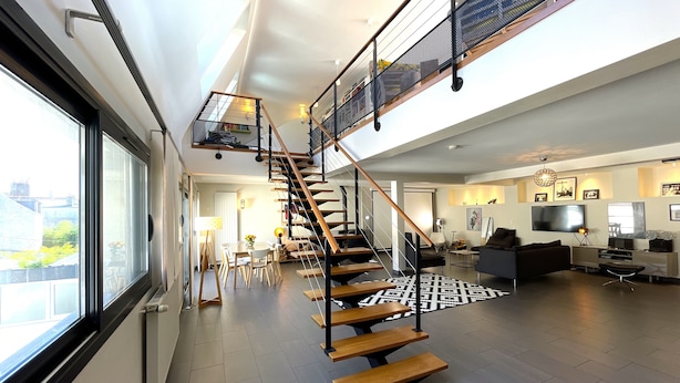 A modern interior with a staircase leading to an upper level, a dining area with a table and chairs, and a living room with a sofa and entertainment unit. - Le loft Concarneau (Concarneau)