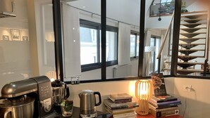 A kitchen with a coffee maker, kettle, and blender on the counter. There are books stacked on a red cabinet and a lamp on the counter. - Le loft Concarneau (Concarneau)