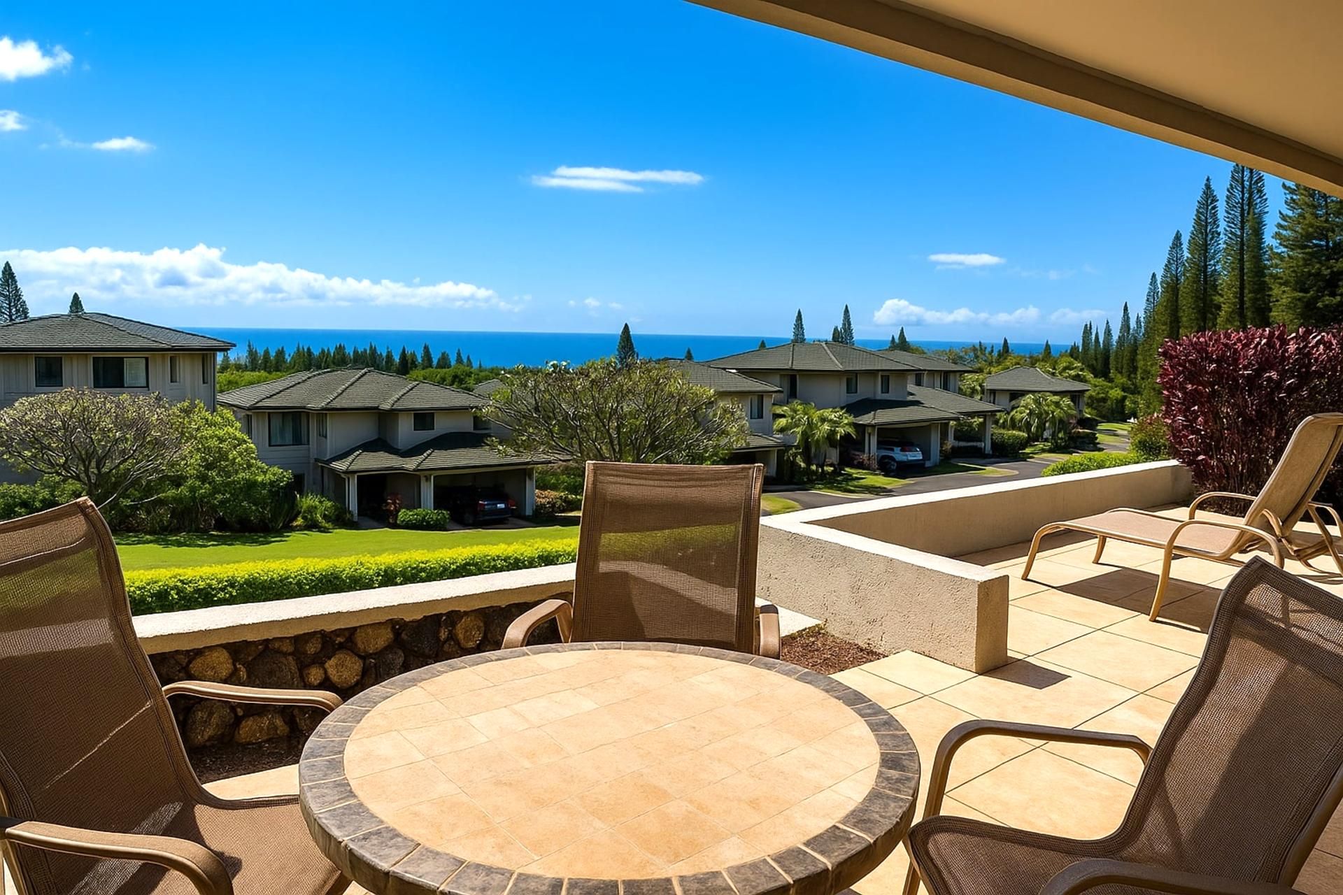 A patio with a round table and chairs, overlooking a residential area with houses and a view of the ocean.