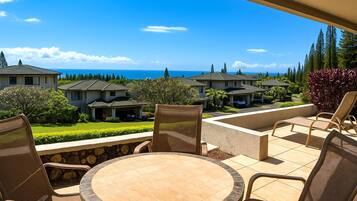 A patio with a round table and chairs, overlooking a residential area with houses and a view of the ocean.