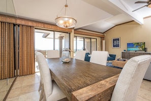 A spacious dining area with a wooden table, white chairs, a chandelier, and a view of the outdoors.
