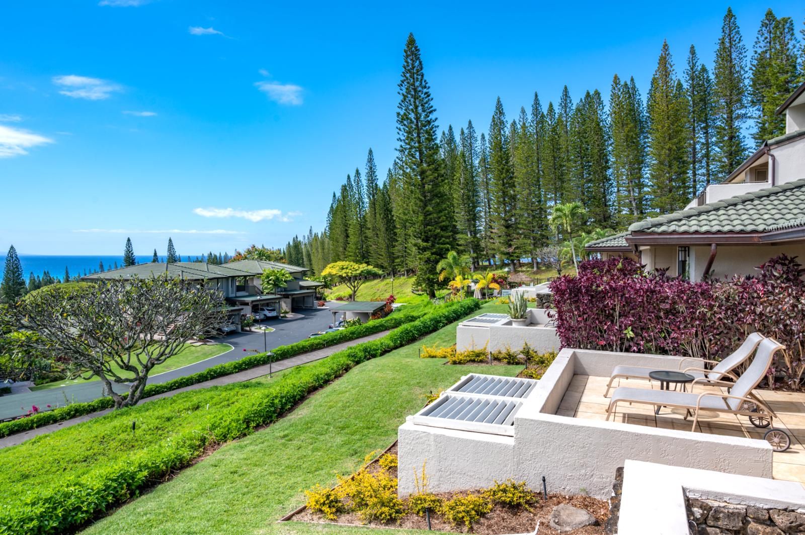 A residential area with a view of the ocean, a driveway, and a patio with outdoor furniture.