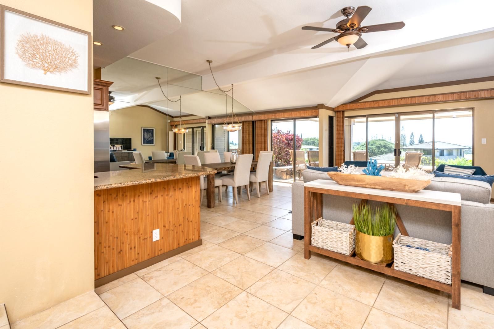 A spacious kitchen with a wooden island, dining area with chairs, a sofa, and large windows offering a view.