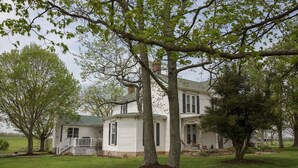 A two-story white house with a porch and a covered front porch area. - Welcome Hall 5 bedroom 1880’s home on 55 acres (Paris)