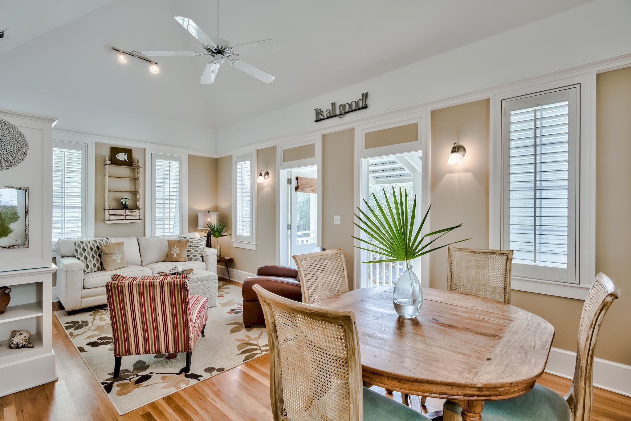 A spacious living room with a large wooden dining table, wicker chairs, and a ceiling fan.