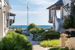 A coastal residential area with a clear view of the sea, a flagpole, and a pathway leading to a house with a balcony.
