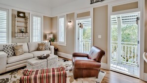 En stue med en beige sofa, en brun læderstol og en stribet skammel. Der er en dekorativ reol med et fiskesymbol og en vægmonteret lampe.