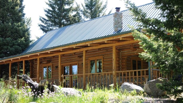 A log cabin with a covered porch, stone chimney, and surrounded by rocks and wildflowers. - Secluded mountain hideaway just outside of Bozeman (Bozeman)