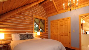 A log cabin bedroom with a large bed, wooden walls, a window, and a chandelier. - Secluded mountain hideaway just outside of Bozeman (Bozeman)