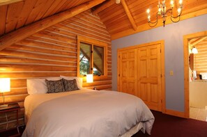Cozy bedroom with a large bed, wooden walls, and a window offering a view of the surrounding greenery.