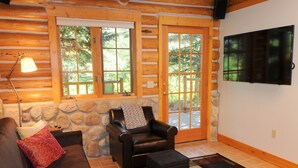 A log cabin interior with a stone wall, a leather chair, a sofa, a lamp, and a television. - Secluded mountain hideaway just outside of Bozeman (Bozeman)