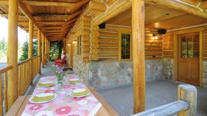A log cabin with a covered porch, stone walls, and a dining area set up with tables and chairs. - Secluded mountain hideaway just outside of Bozeman (Bozeman)