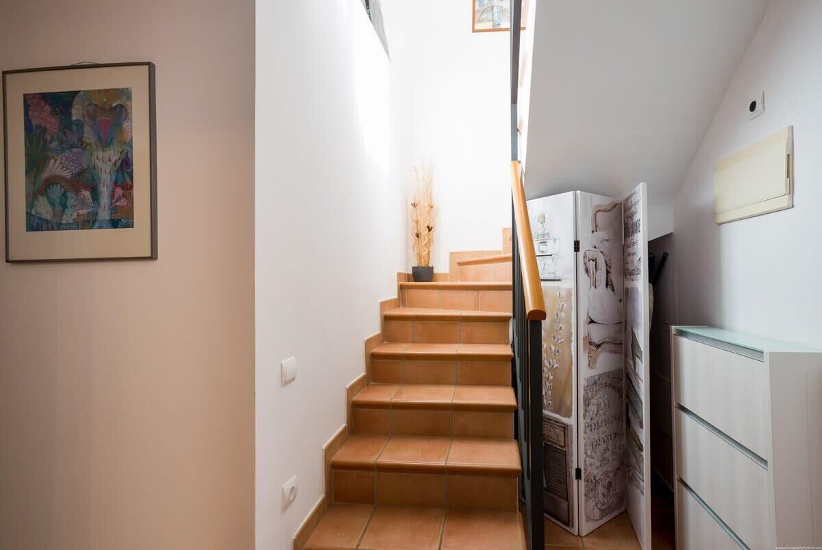 Eine Treppe mit Handlauf, ein gerahmtes abstraktes Gemälde an der Wand und ein weißes Schränkchen mit Schubladen.