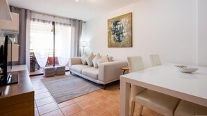 A modern living room with a sofa, a dining table, and a painting on the wall. - GO2TENERIFE Apart'Tera Solarium, Terraces, Swimming pools & Parking (Adeje)