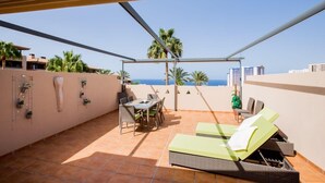 A terrace with a table and chairs, a lounge area with sun loungers, and a view of the ocean. - GO2TENERIFE Apart'Tera Solarium, Terraces, Swimming pools & Parking (Adeje)