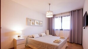 A bedroom with a bed, bedside tables, a lamp, a TV, and a window with curtains. - GO2TENERIFE Apart'Tera Solarium, Terraces, Swimming pools & Parking (Adeje)