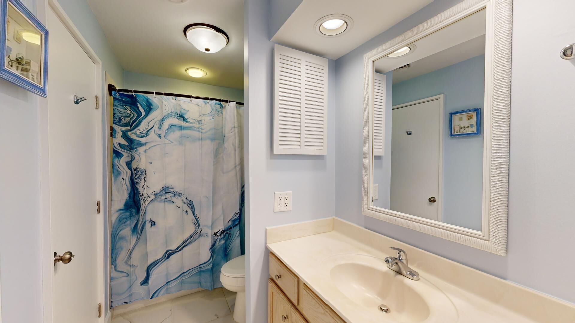 A bathroom with a marble shower curtain, a sink with a mirror, and a toilet.