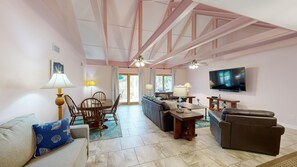 Relax in this spacious living area with a high ceiling, featuring a sofa, loveseat, dining table, and flat-screen TV.