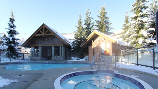 Ein Poolbereich mit Whirlpool, umgeben von schneebedeckten Bäumen und einer Lodge mit Holzfassade.