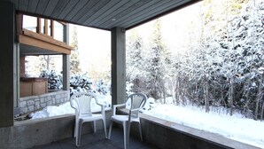 Eine überdachte Terrasse mit zwei weißen Plastikstühlen und einem Tisch, mit Blick auf eine verschneite Landschaft mit Bäumen.