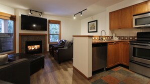 Eine moderne Küche mit Kamin, Holzsäulen, Edelstahlgeräten und einem flachbildfernseher über dem Kamin.