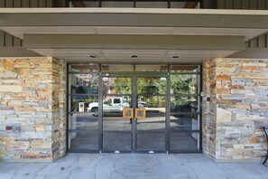 Entrada de un edificio con muros de piedra, un puerta de cristal y un estacionamiento visible a través de la puerta.