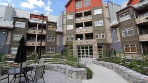 Un edificio residencial de varios pisos con balcones, fachada de piedra y un patio con mobiliario exterior.