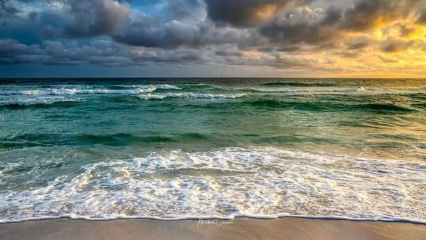 Une plage avec des vagues et un ciel nuageux.