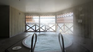 A hot tub in a room with a view of a building through a window with a lattice design.