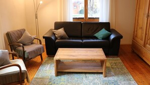 Ett vardagsrum med en svart lädersoffa, ett soffbord i trä och en golvlampa.