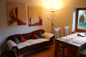 Relax in this inviting living room with a sofa, dining table, and chairs, plus a floor lamp and wall art.