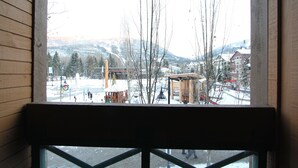 A view through a window of a building with a wooden exterior, overlooking a snowy landscape with buildings and trees.